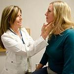 Female physician assistant checking the neck glands of a female patient.